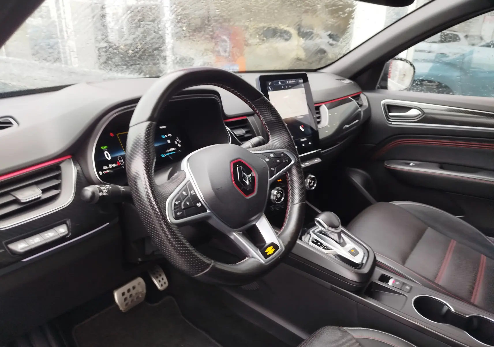 Vue intérieure côté conducteur du Renault Arkana 1.6 E-Tech bleu Zanzibar, volant sport avec surpiqûres rouges et écran tactile central.