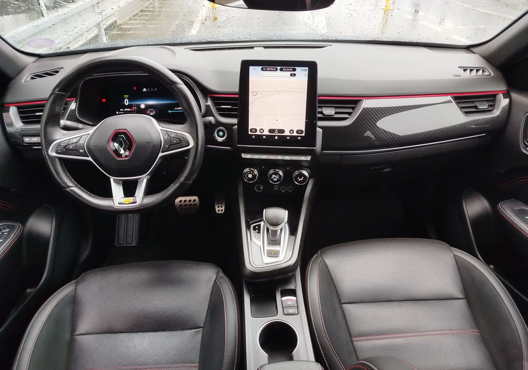 Vue intérieure avant du Renault Arkana 1.6 E-Tech 145ch RS Line 2022, tableau de bord noir avec touches rouges et écran tactile central.