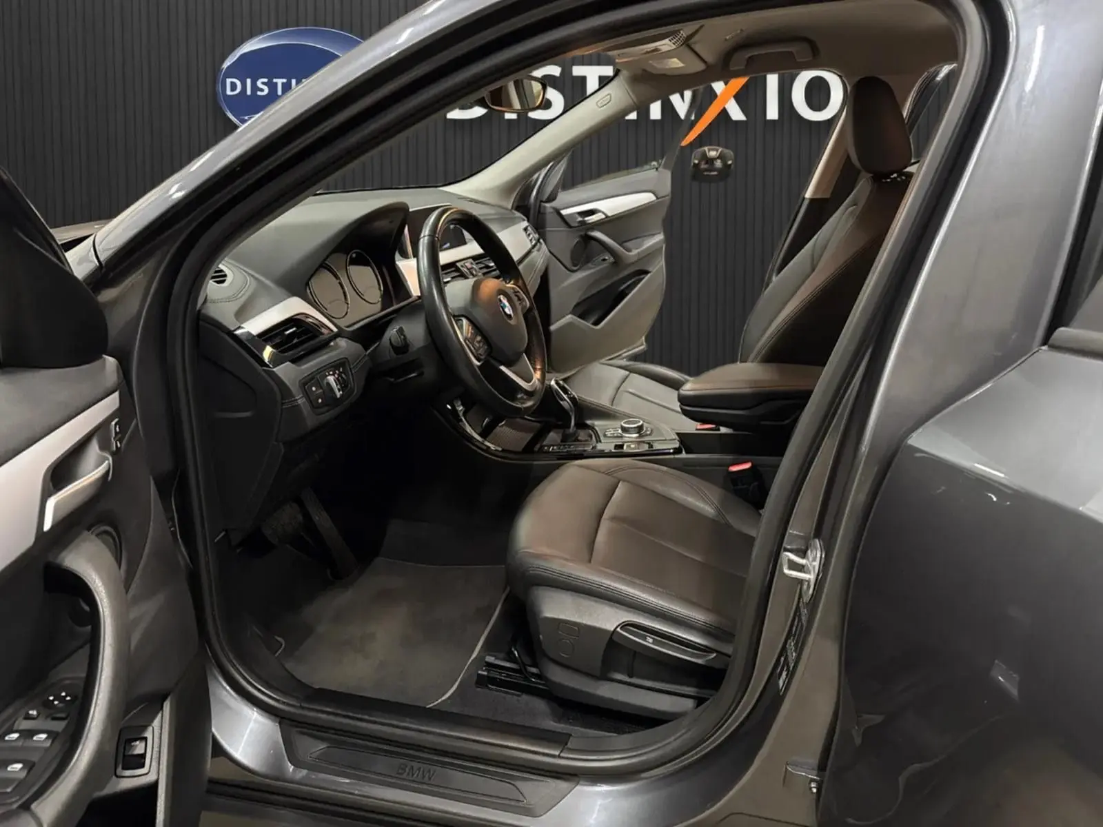 Vue intérieure côté conducteur d’un BMW X2 gris minéral métallique de 2019 avec sièges cuir noir et tableau de bord moderne.