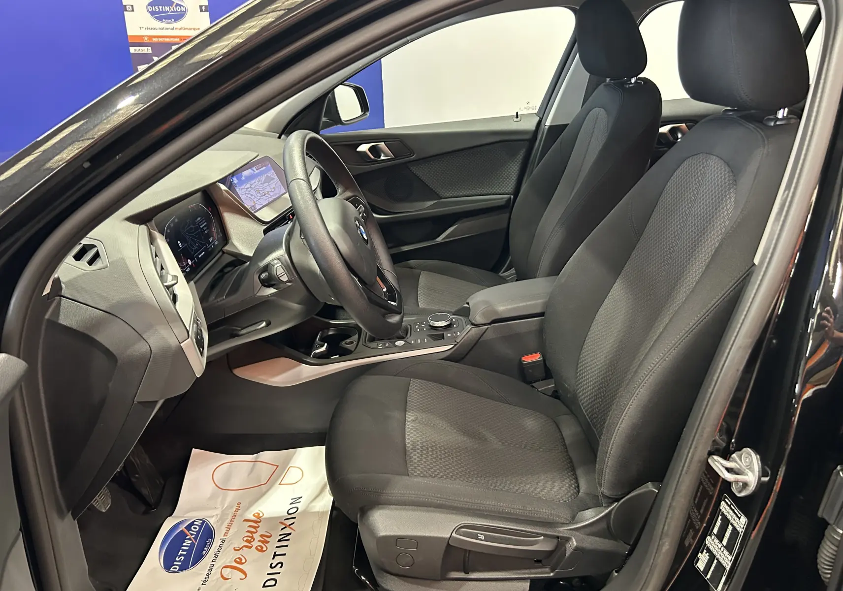 Vue intérieure côté conducteur de la BMW Série 1 noire 2023 avec sièges tissu et tableau de bord digital.