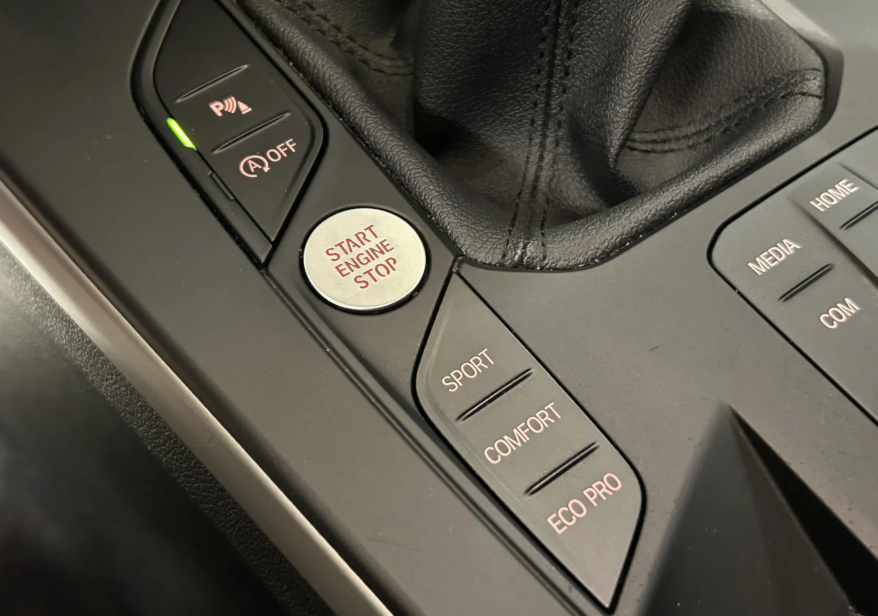 Gros plan sur la console centrale noire de la BMW Série 1 16d 2023, montrant les boutons de mode de conduite et le démarrage moteur.