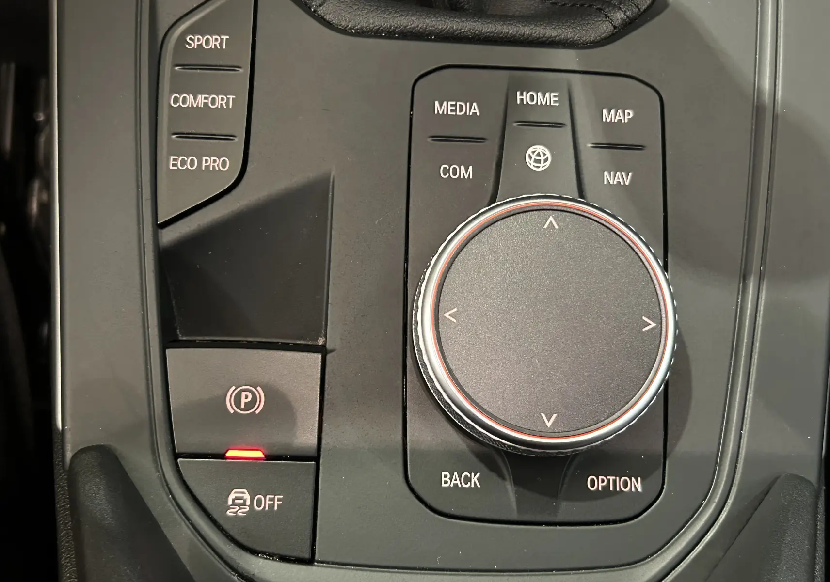 Gros plan sur la molette de commande centrale et les boutons de modes de conduite dans l'habitacle noir d'une BMW Série 1 16d 2023.