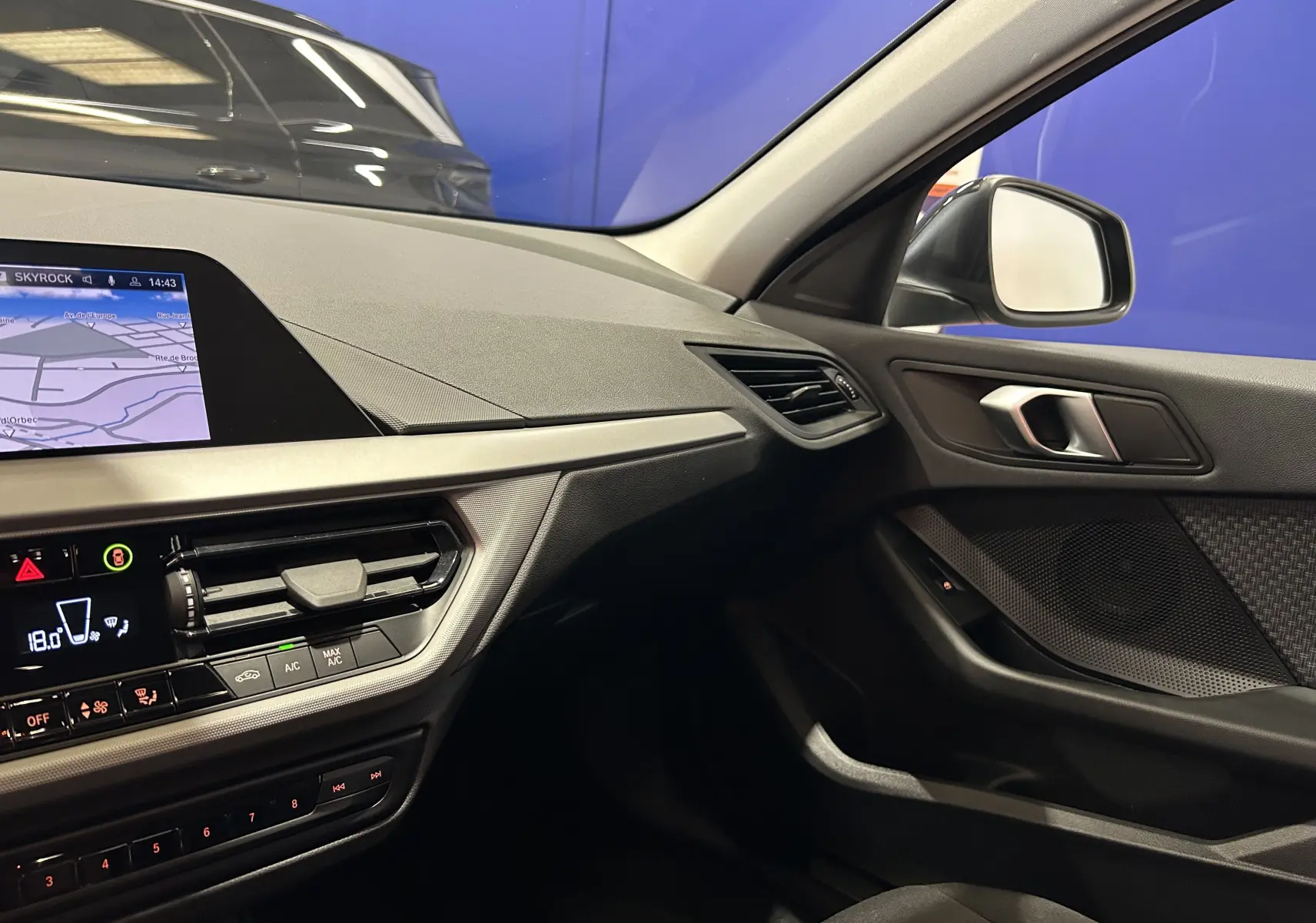 Vue intérieure côté passager de la BMW Série 1 noire 2023, mettant en valeur le tableau de bord avec GPS et les finitions modernes.