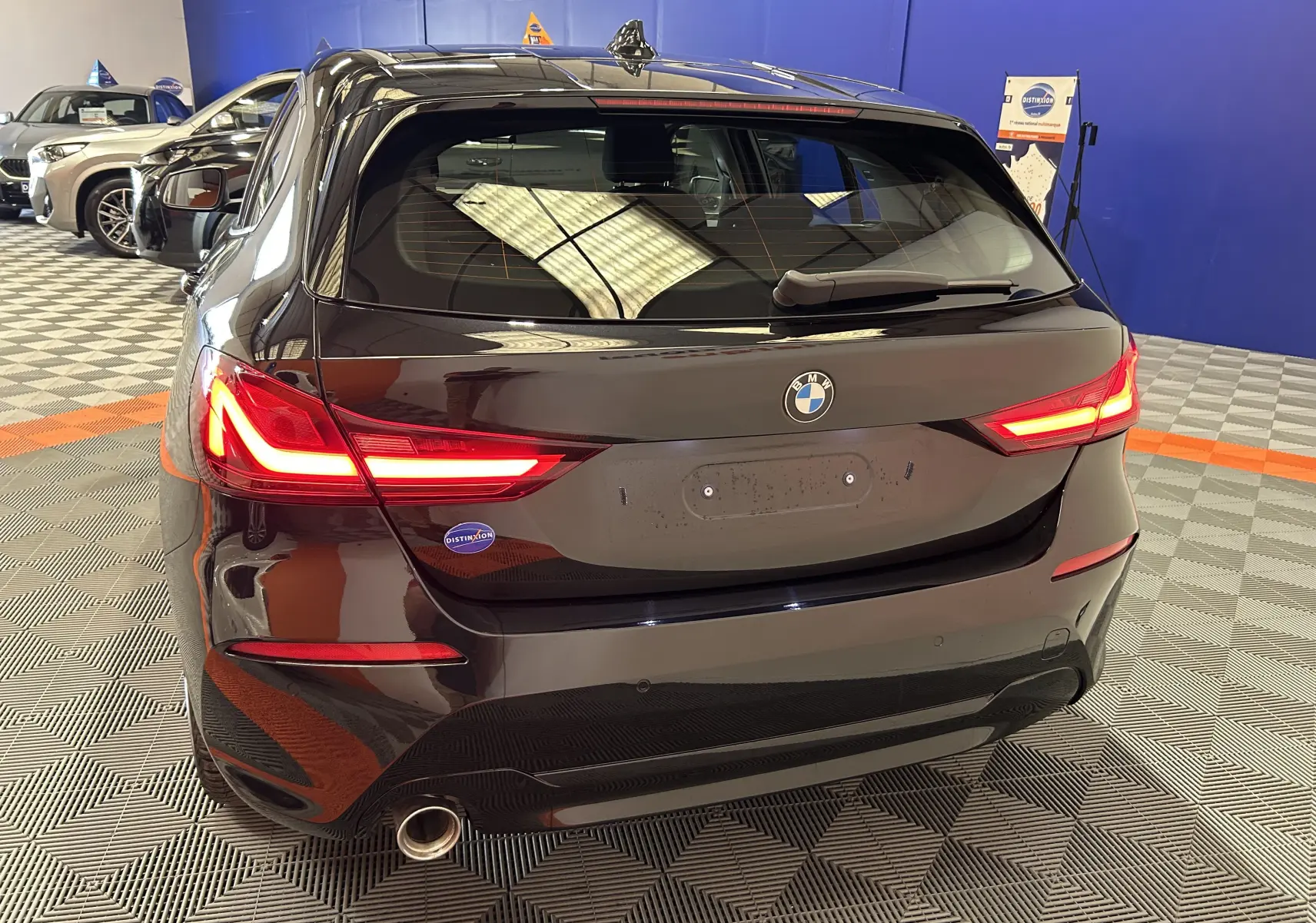 Vue arrière d'une BMW Série 1 noire 16d 116ch avec feux LED allumés dans un showroom intérieur.