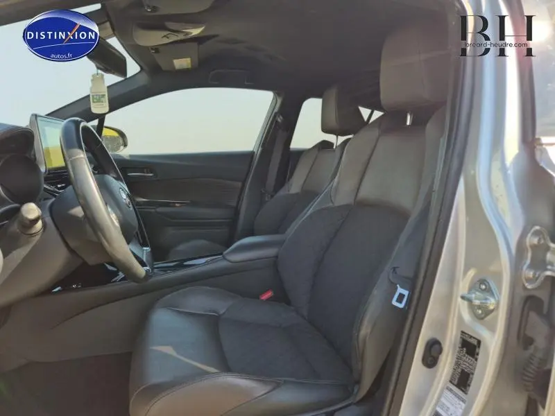 Vue intérieure côté conducteur du Toyota C-HR gris aluminium 2019, sièges mi-cuir chocolat avec surpiqûres et volant cuir multifonction.