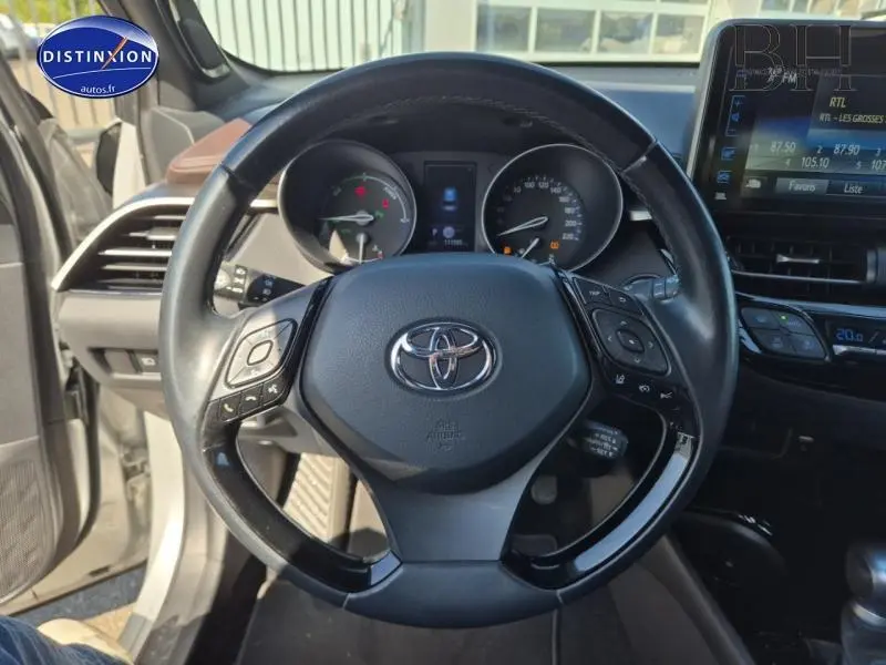 Vue rapprochée du volant cuir multifonction noir du Toyota C-HR gris aluminium avec tableau de bord et écran tactile visible.