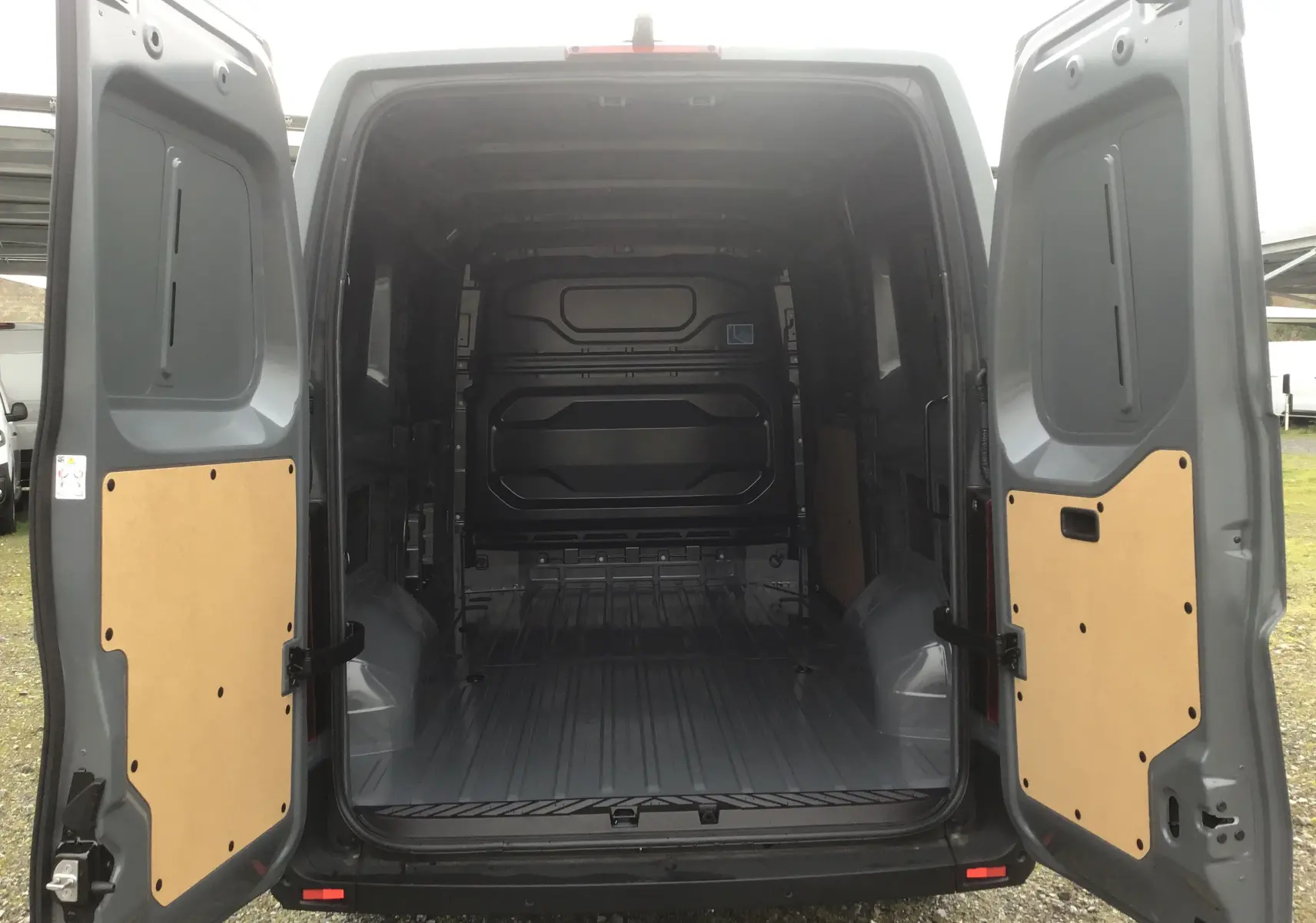Vue arrière ouverte du Renault Master gris urbain 2025, montrant l’espace de chargement vide avec panneaux bois sur portes.