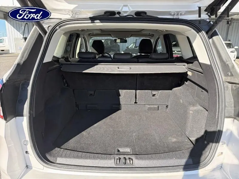 Coffre ouvert vu de l'arrière d'un Ford Kuga blanc avec cache-bagages et intérieur noir.