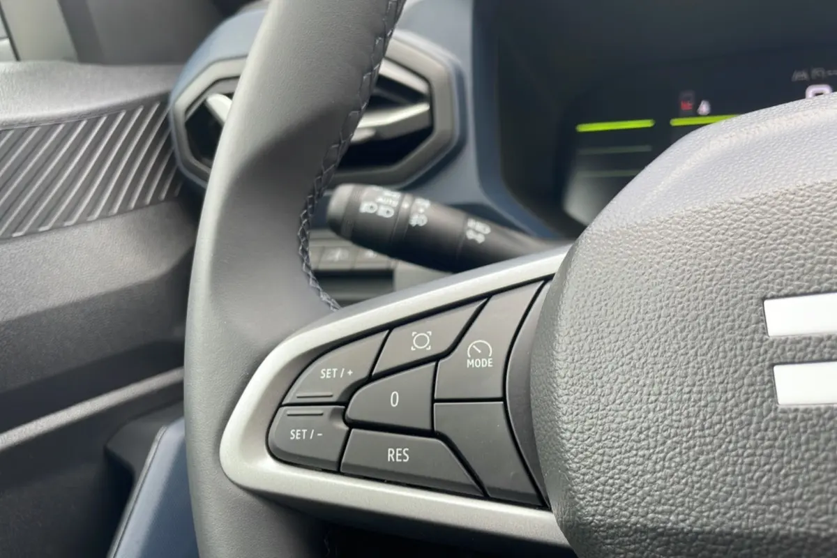 Gros plan sur les commandes au volant cuir du DACIA BIGSTER 2025, version gris schiste, côté gauche du volant.