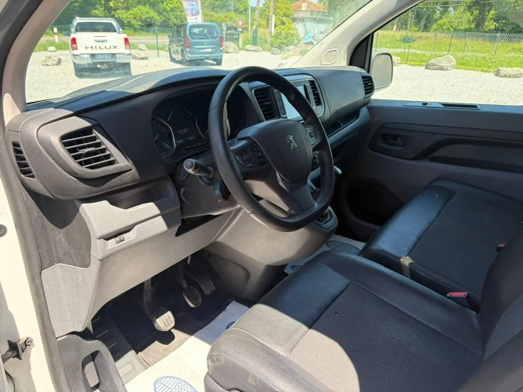 Vue intérieure côté conducteur du Peugeot Expert Fourgon blanc 2019, volant cuir multifonctions et sièges en tissu noir.