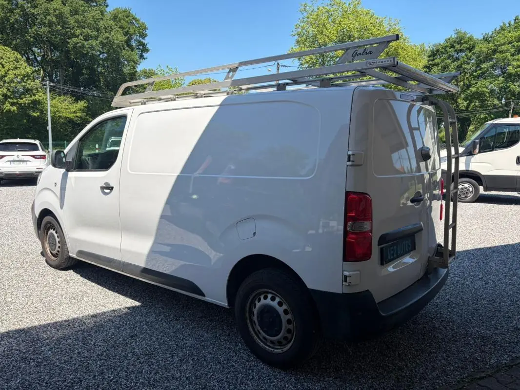 Vue 3/4 arrière gauche du fourgon blanc Peugeot Expert L1H1 Confort avec galerie de toit et porte-échelle arrière.