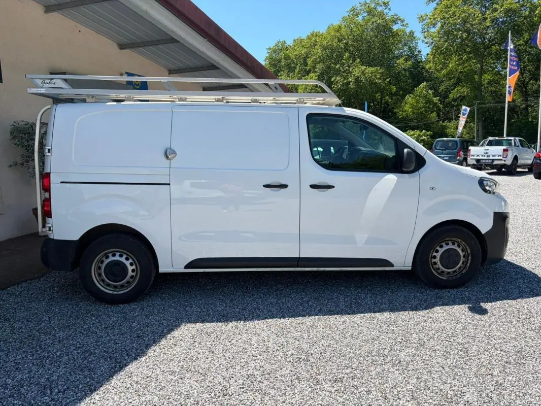 Peugeot Expert Fourgon blanc en vue de profil côté gauche, avec galerie de toit et portes coulissantes fermées.