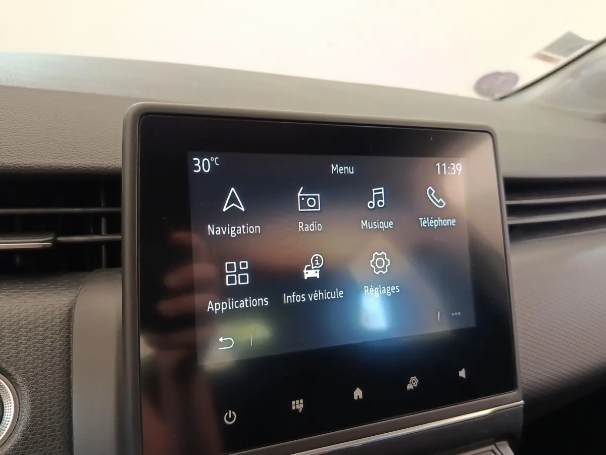 Écran tactile central de la Renault Clio Business gris clair, affichant le menu principal avec navigation et radio.