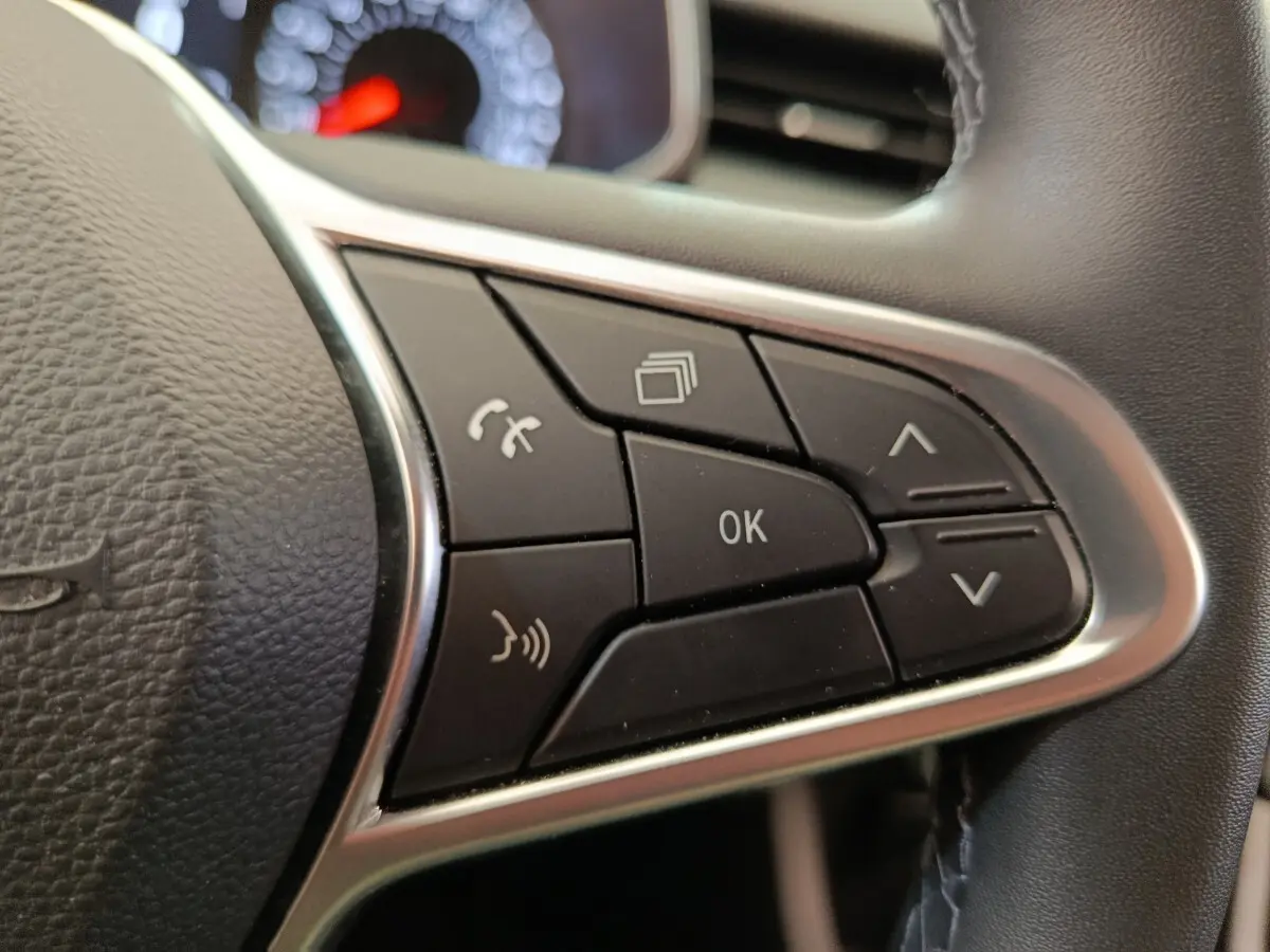 Gros plan sur les commandes multifonctions noires du volant cuir synthétique d’une Renault Clio Business gris clair.