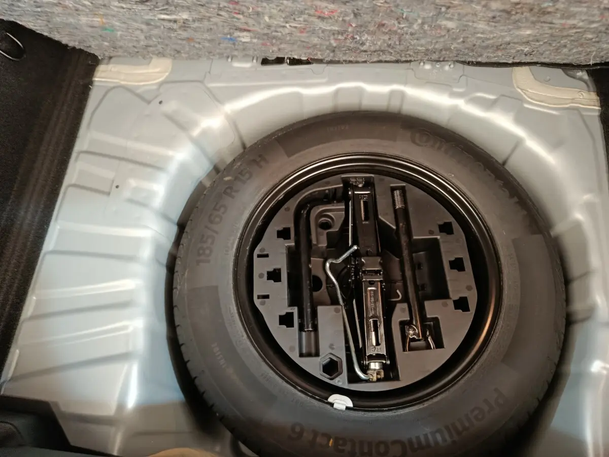 Vue plongeante sur la roue de secours et les outils de bord dans le coffre d'une Renault Clio gris clair.