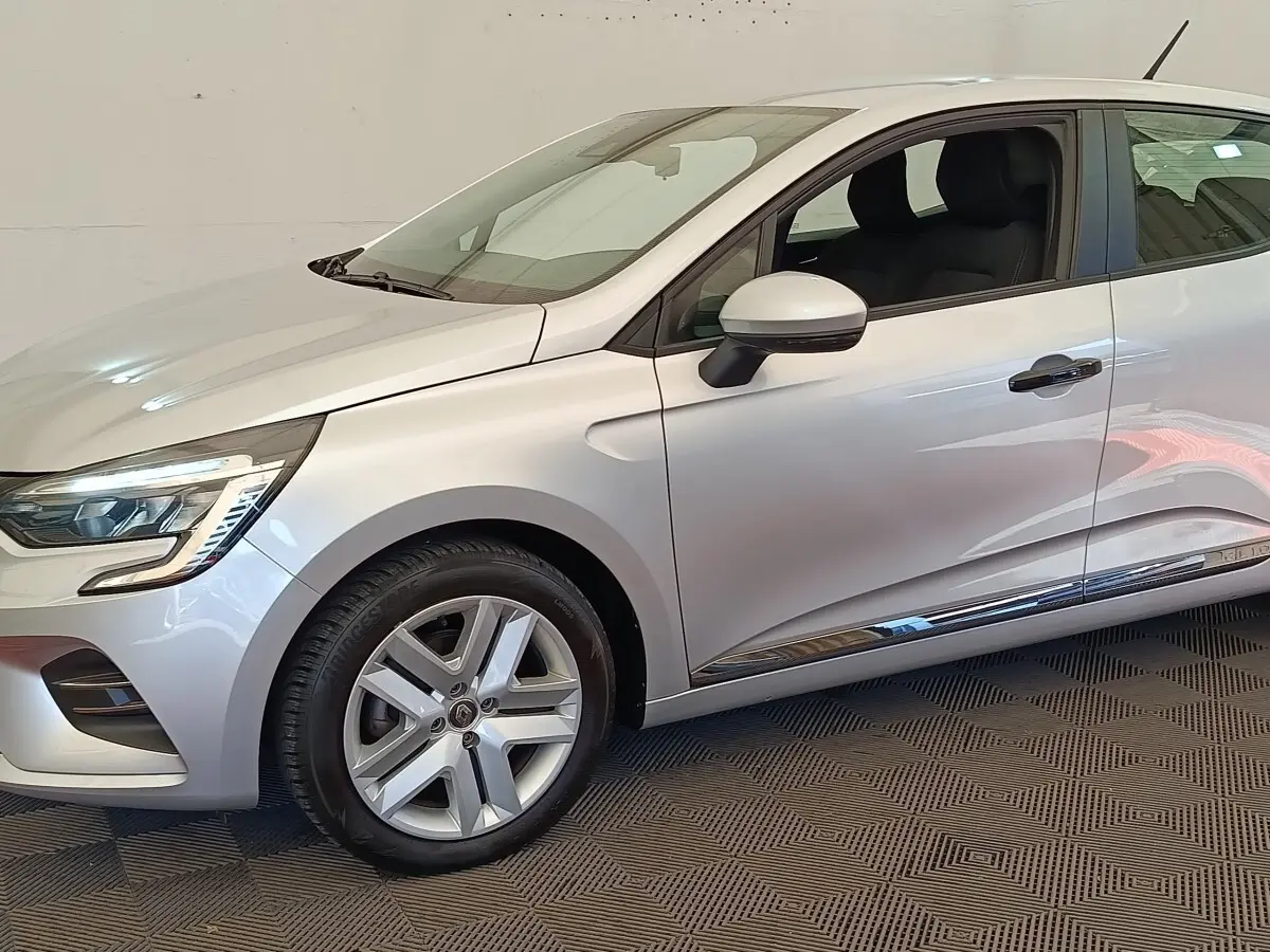 Vue de profil côté gauche d'une Renault Clio Business TCe 100 gris clair avec jantes alliage et feux LED avant visibles.
