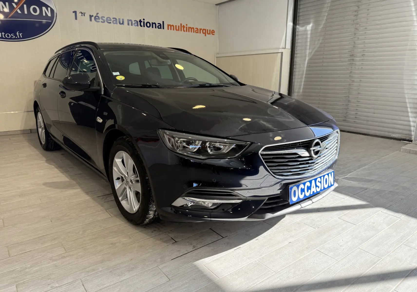 Vue 3/4 avant d'une Opel Insignia Sports Tourer bleu lune marine métal avec calandre chromée en showroom.