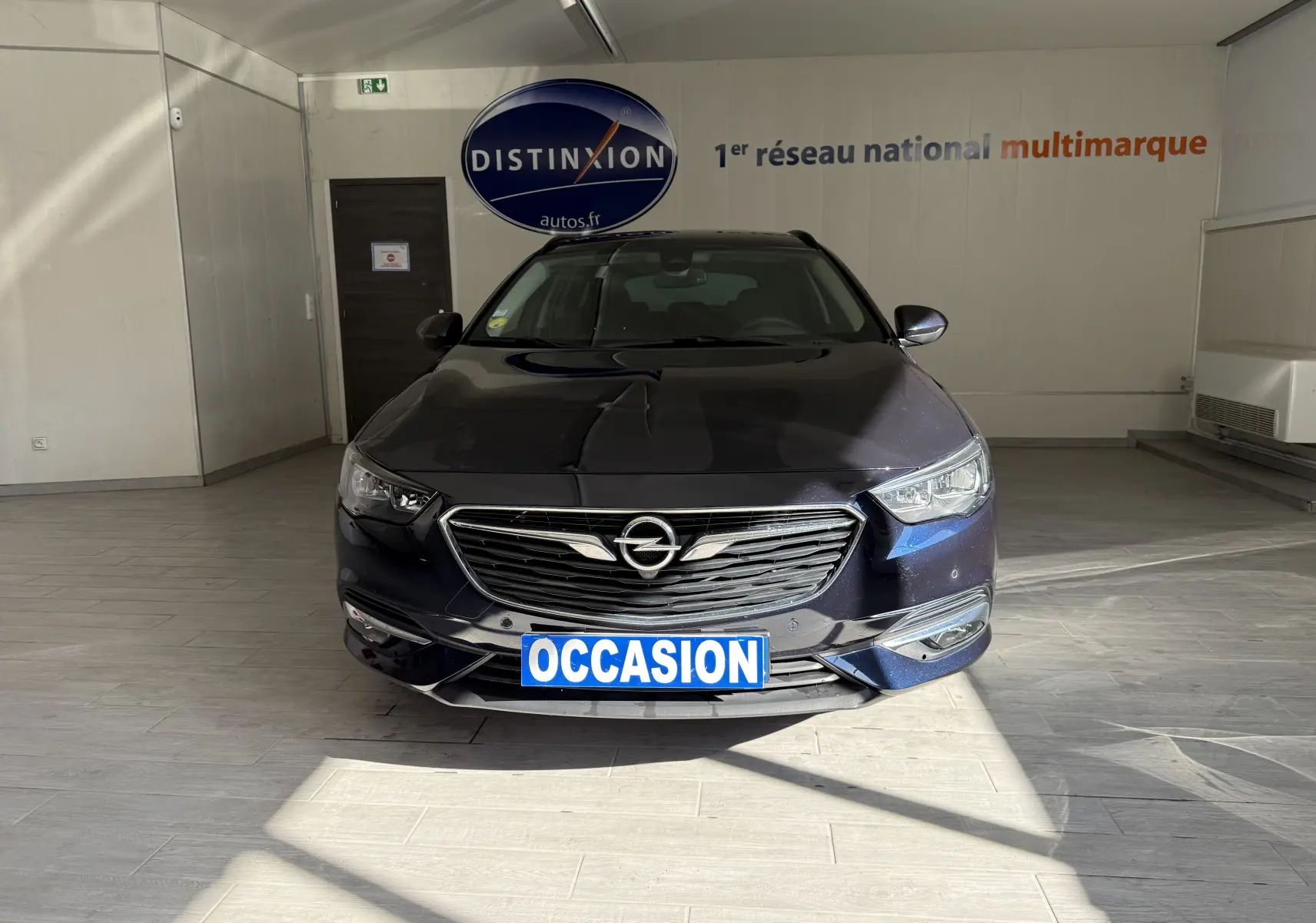 Vue frontale d'une Opel Insignia Sports Tourer bleu lune marine métal avec calandre chromée et plaque "OCCASION" visible.