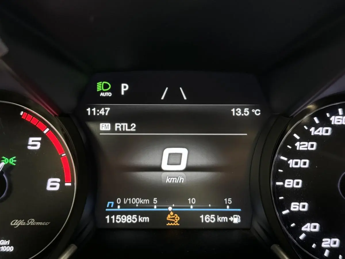 Tableau de bord numérique de l'Alfa Romeo Giulia gris, affichant 0 km/h et 115985 km au compteur.