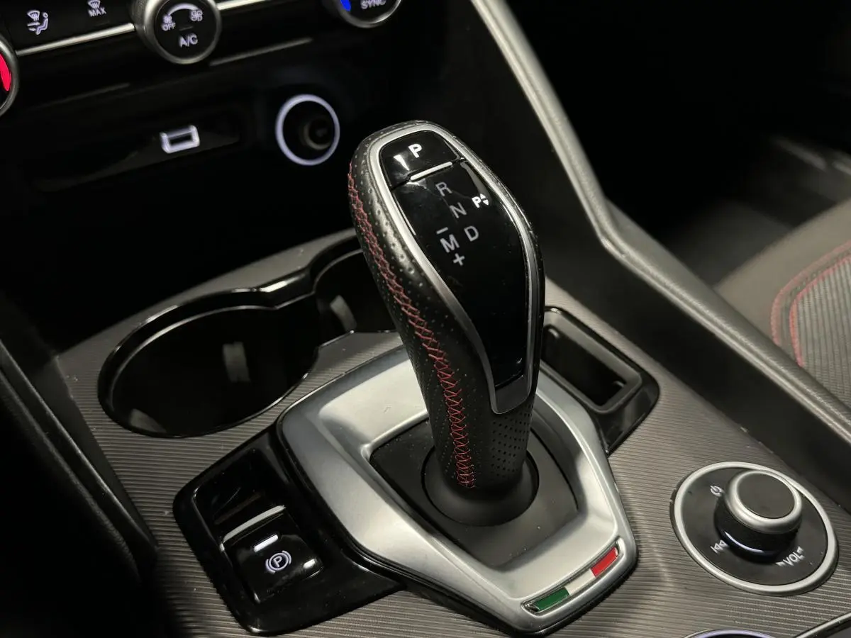 Gros plan sur la commande de boîte automatique avec surpiqûres rouges dans l’habitacle noir de l’Alfa Romeo Giulia gris 2021.