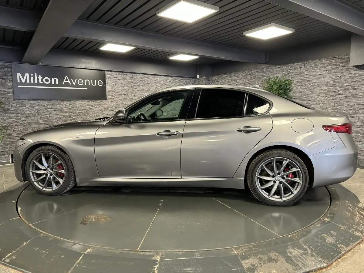 Profil droit d'une Alfa Romeo Giulia gris métallisé avec jantes alliage 18 pouces et vitres arrière surteintées dans un showroom.