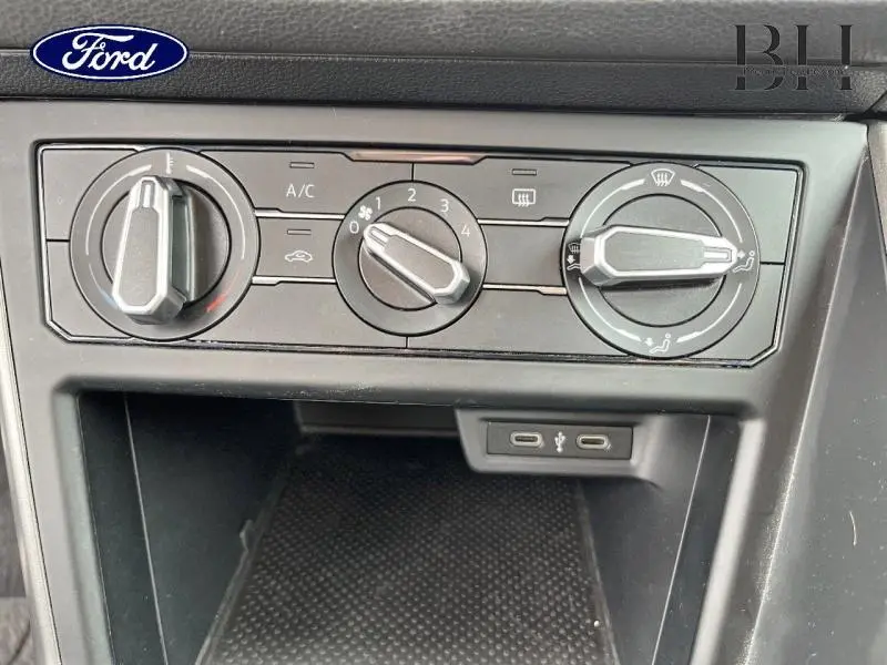 Gros plan sur les commandes de climatisation grises d'une Volkswagen Polo blanche, avec deux ports USB visibles en dessous.