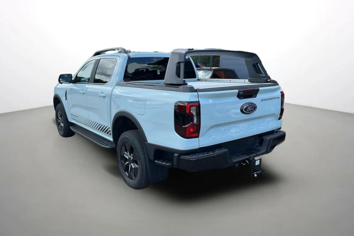 Vue 3/4 arrière droite du Ford Ranger 2.3 PHEV Stormtrak 2026 en bleu clair avec arceau sport et attelage.