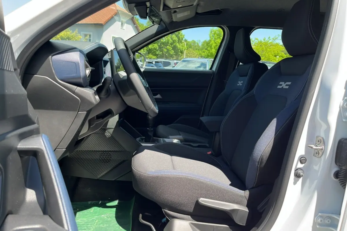 Intérieur côté conducteur du Dacia Bigster blanc glacier 2025, sièges tissu avec logo, volant cuir et levier de vitesses manuel.