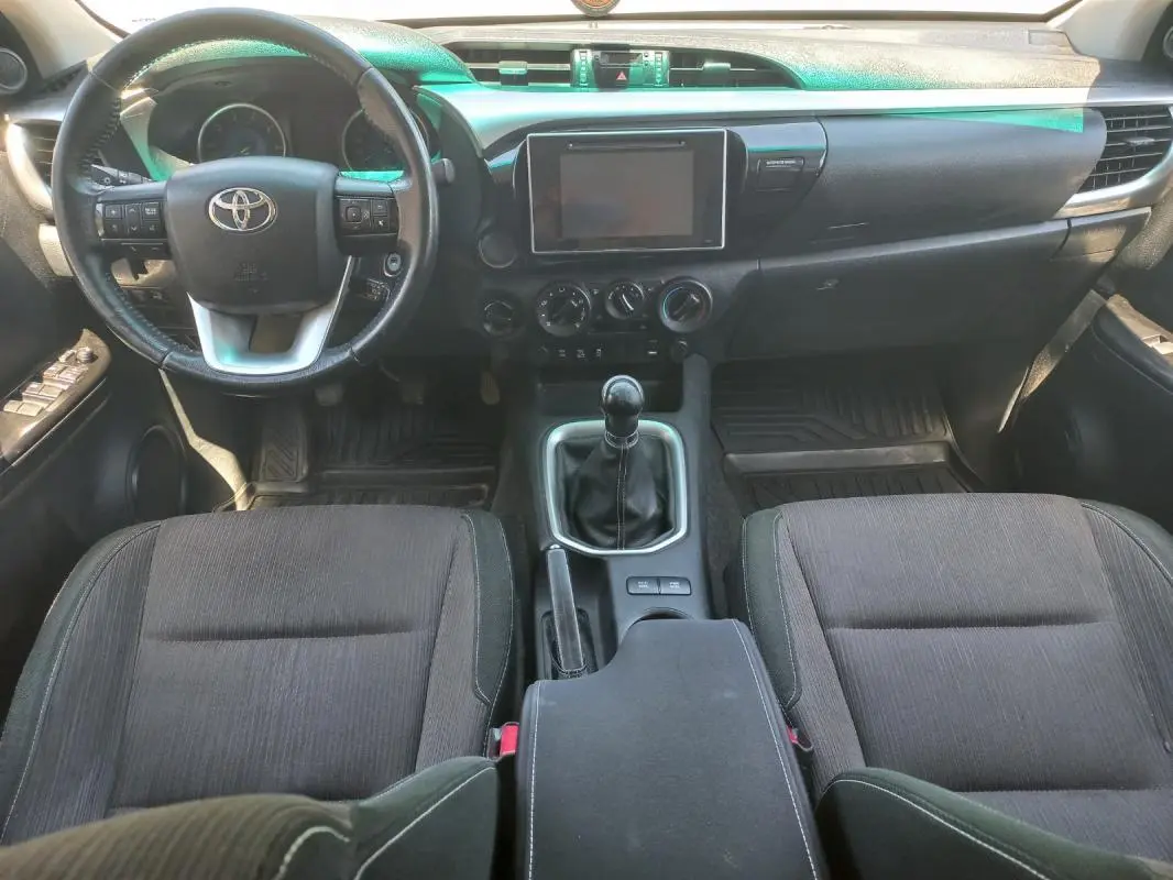 Vue intérieure avant du Toyota Hilux 2018, tableau de bord noir avec volant multifonction et levier de vitesse manuel.