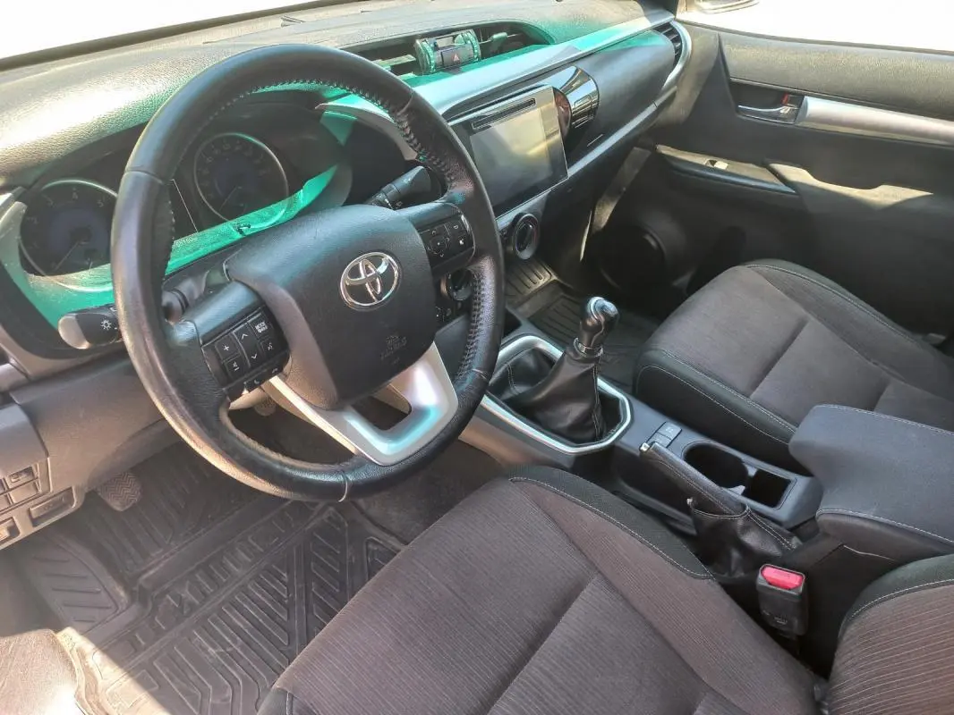 Vue intérieure côté conducteur du Toyota Hilux 2018, montrant le volant, la boîte manuelle et les sièges noirs.