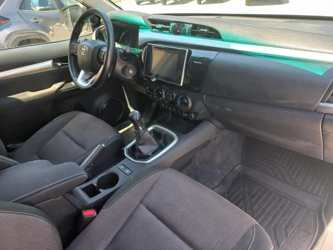 Vue intérieure côté conducteur du Toyota Hilux 2018, montrant le volant, la console centrale avec boîte manuelle et écran tactile.