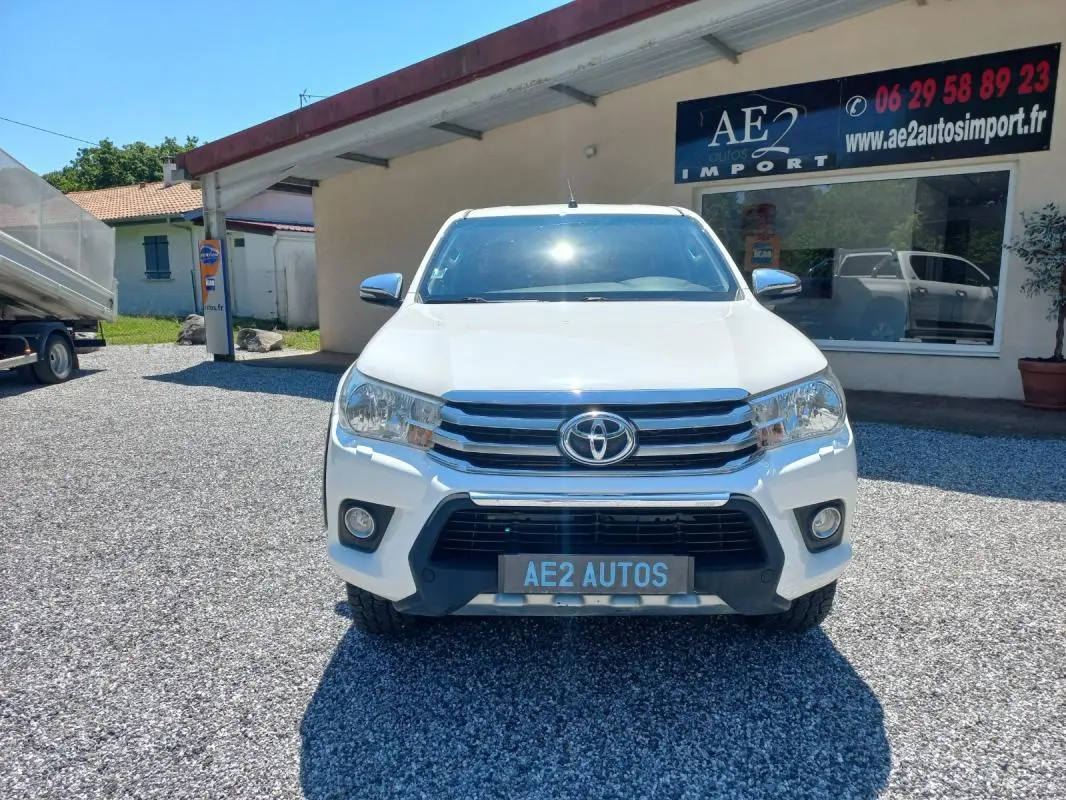 Vue de face du Toyota Hilux blanc 2018, double cabine, avec calandre chromée et plaque AE2 AUTOS.