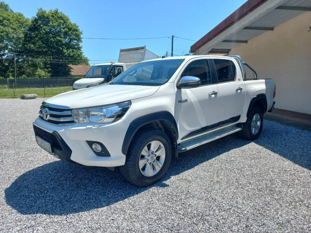 Toyota Hilux 4x4 blanc en 3/4 avant droit, double cabine avec barres de protection et jantes alliage.