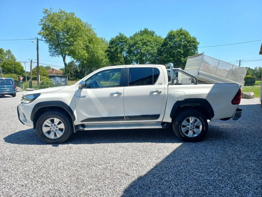 Profil droit du Toyota Hilux 4x4 blanc double cabine 2018 avec barres de protection et benne arrière relevée.