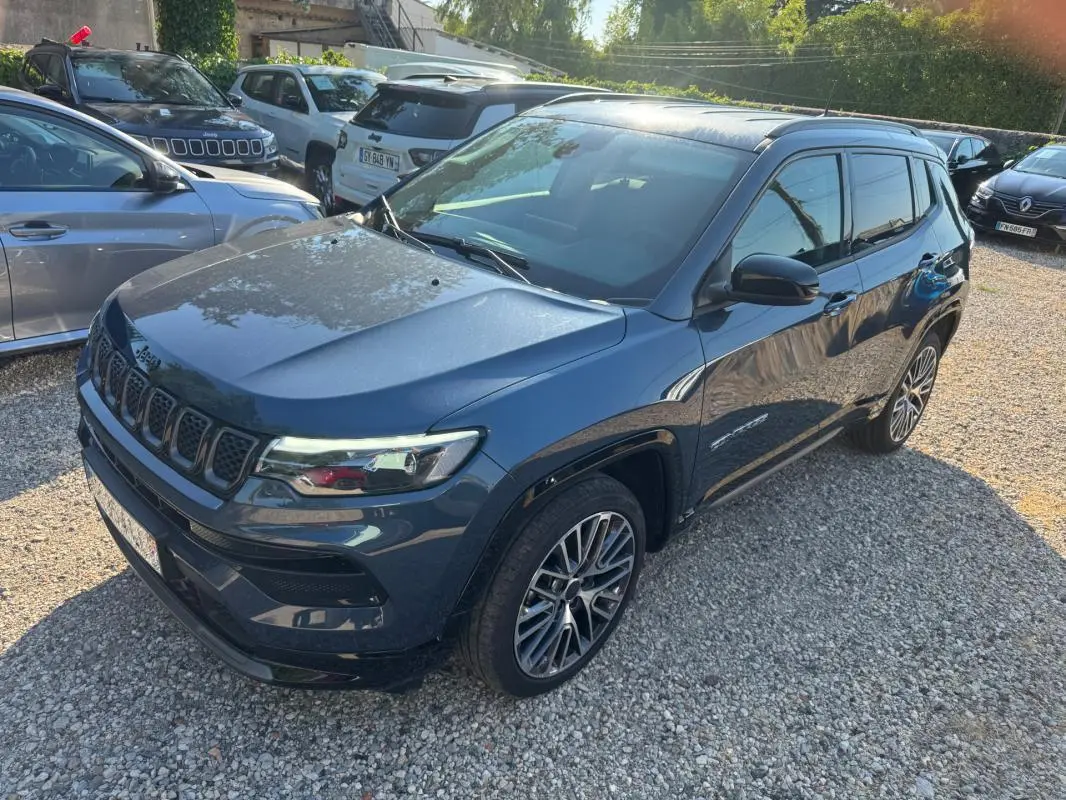 Vue 3/4 avant droite d'un Jeep Compass bleu 2025 avec jantes alliage 19 pouces et barres de toit visibles.