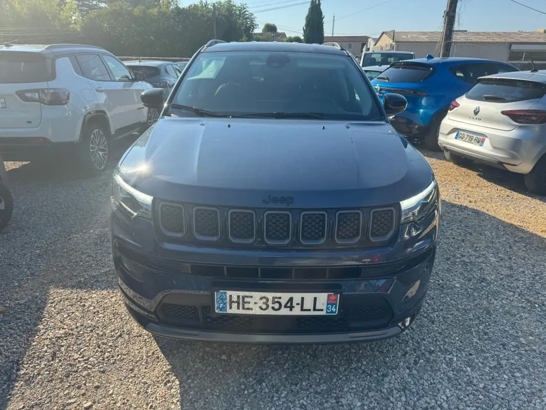 Vue avant d'un Jeep Compass bleu 2025 avec calandre distinctive et barres de toit visibles en extérieur.