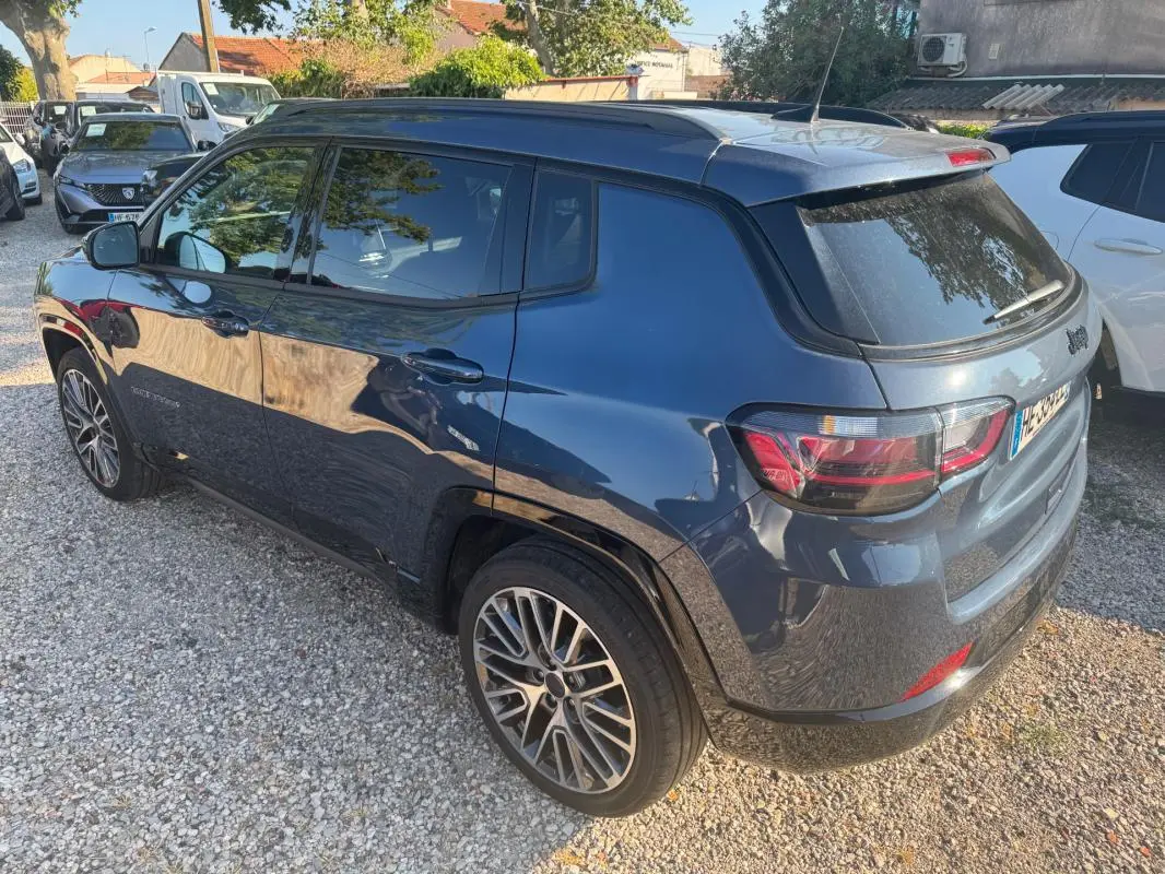 Vue 3/4 arrière droite d'un Jeep Compass bleu 2025 avec jantes alliage 19 pouces et barres de toit visibles.