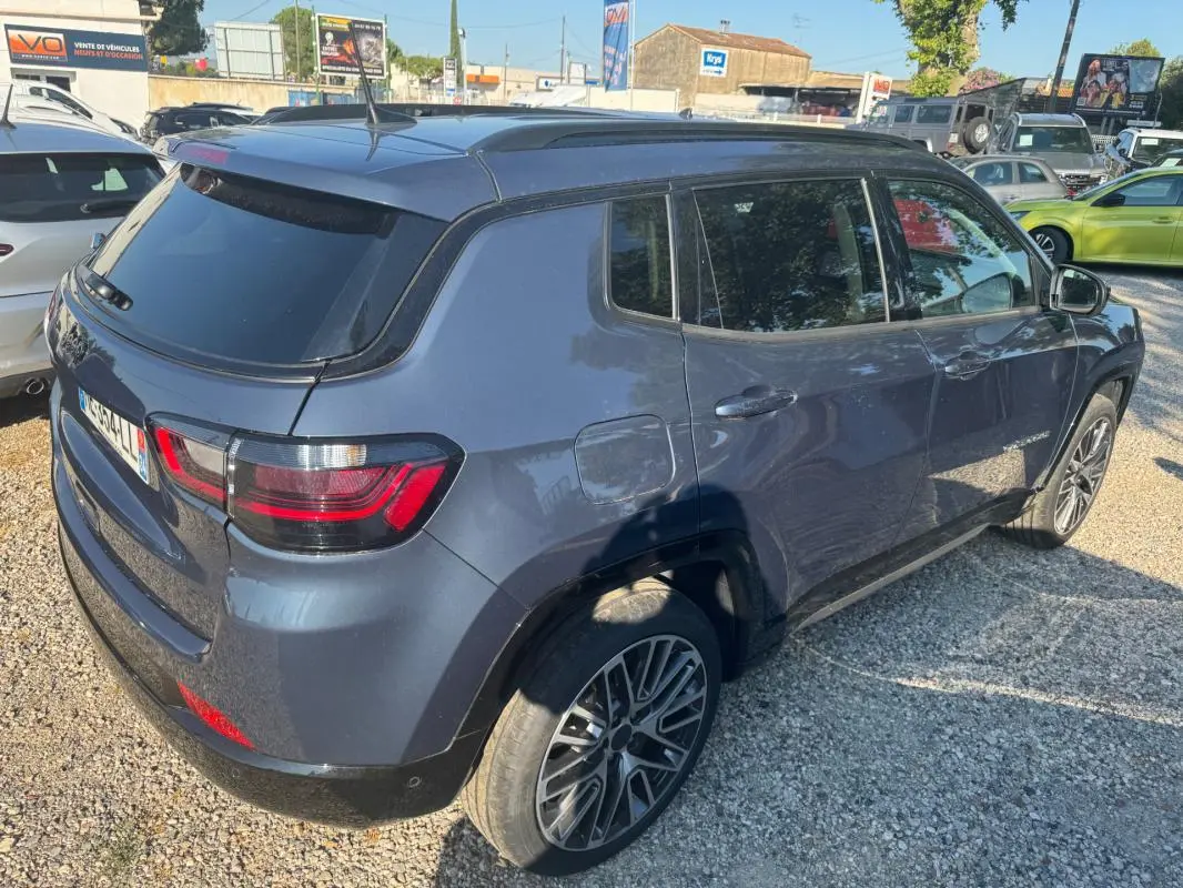Vue 3/4 arrière droite d’un Jeep Compass bleu 2025 avec jantes alliage 19 pouces et barres de toit visibles.