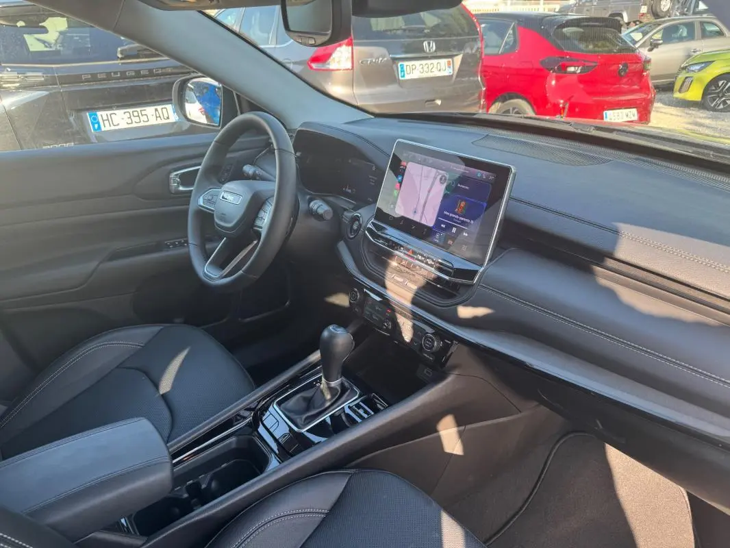 Intérieur avant droit du Jeep Compass bleu 2025, avec écran tactile, volant multifonction et accoudoir central.