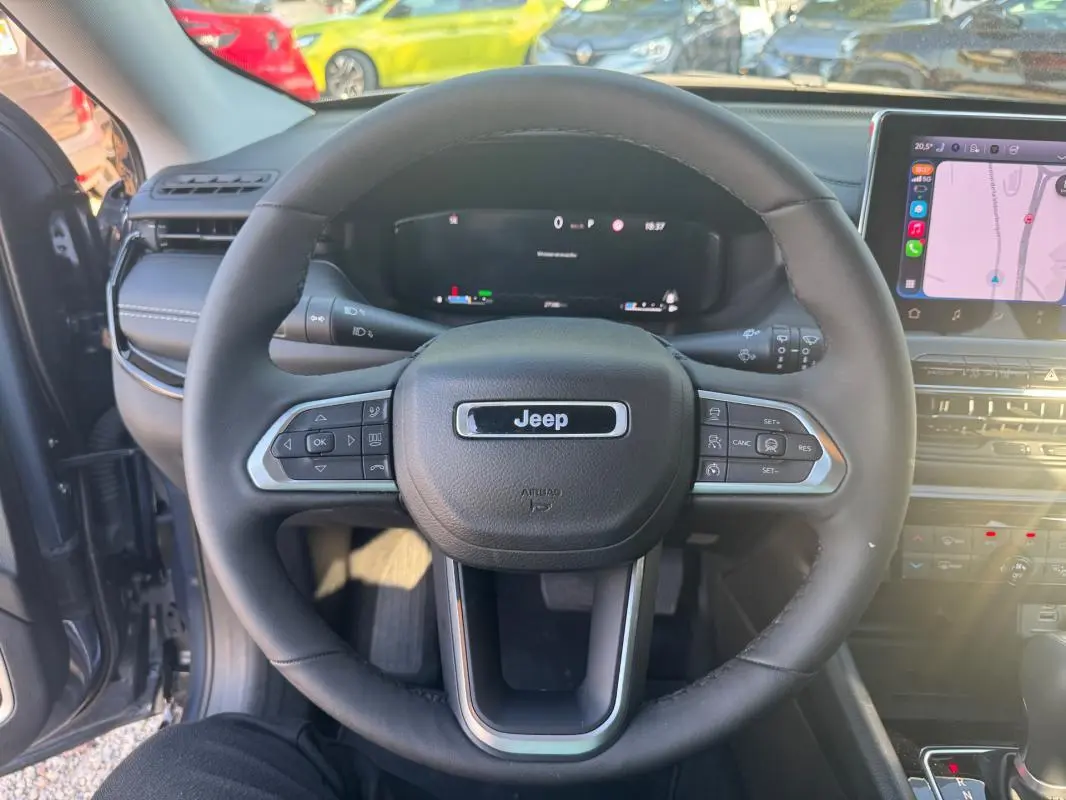 Vue centrée du volant noir du Jeep Compass 2025 bleu, avec tableau de bord numérique et écran tactile visible à droite.