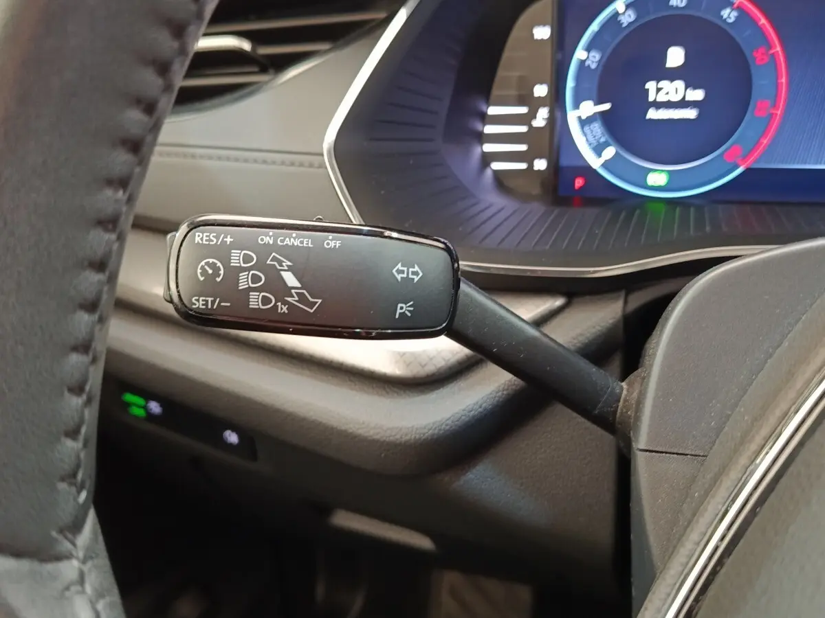 Gros plan sur la manette de régulateur de vitesse à gauche du volant dans l’habitacle sombre d’une Skoda Octavia blanche.