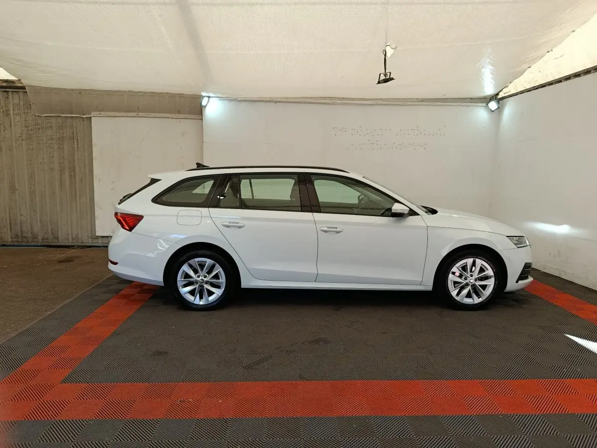 Vue de profil côté gauche d'une Skoda Octavia break blanche 2023 dans un garage avec rails de toit noirs.