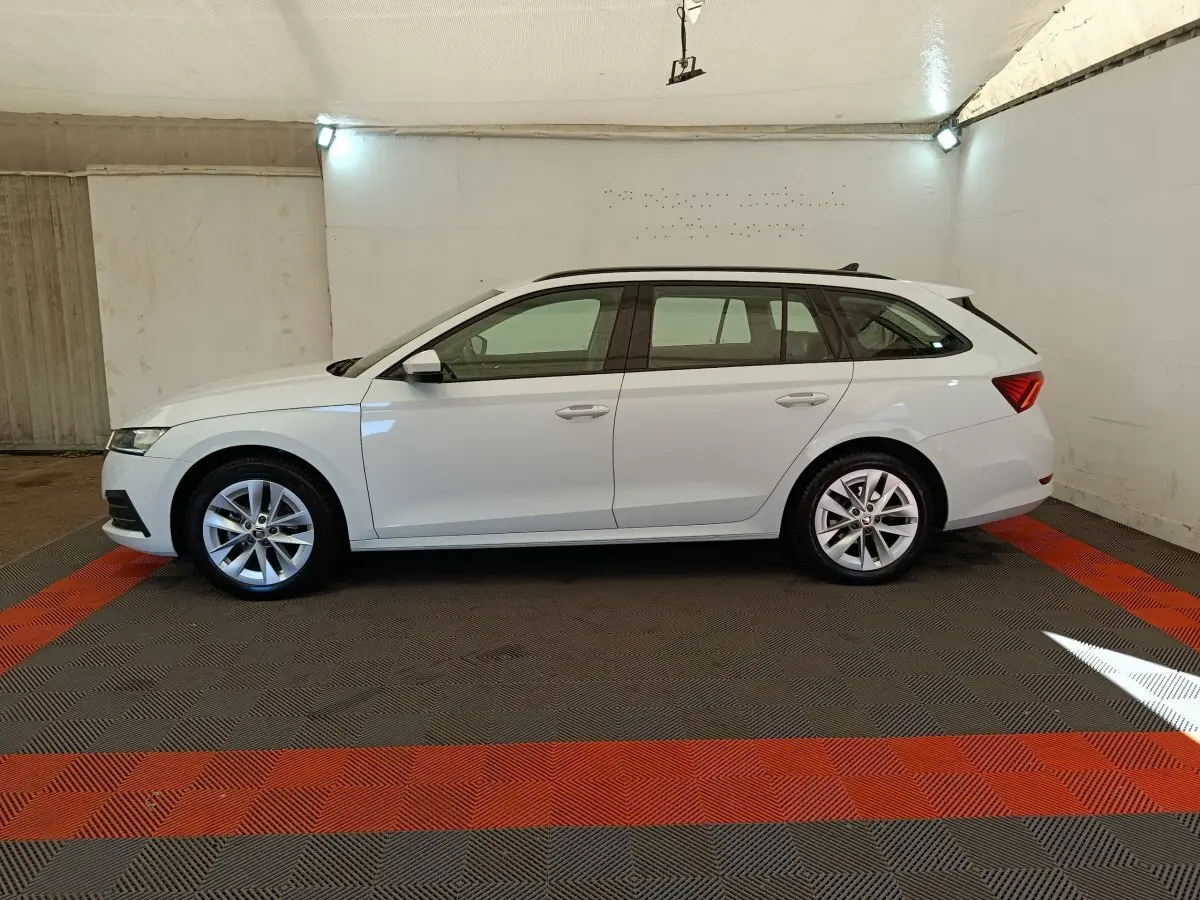 Vue latérale droite d'une Skoda Octavia break blanche 2023 dans un garage avec sol à motifs gris et rouge.
