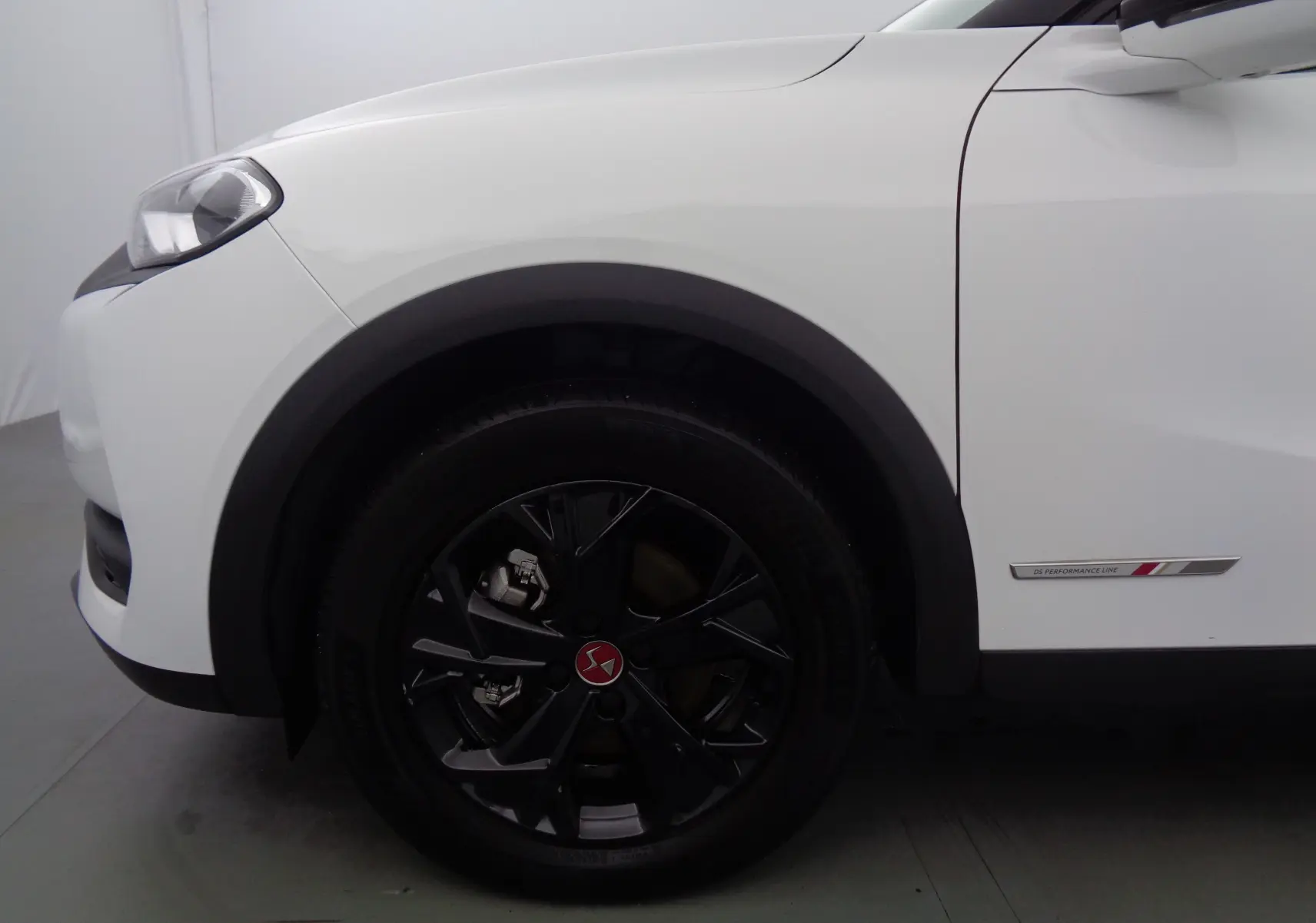 Gros plan sur la roue avant gauche noire et la carrosserie blanche banquise d'un DS3 Crossback avec badge Performance Line.