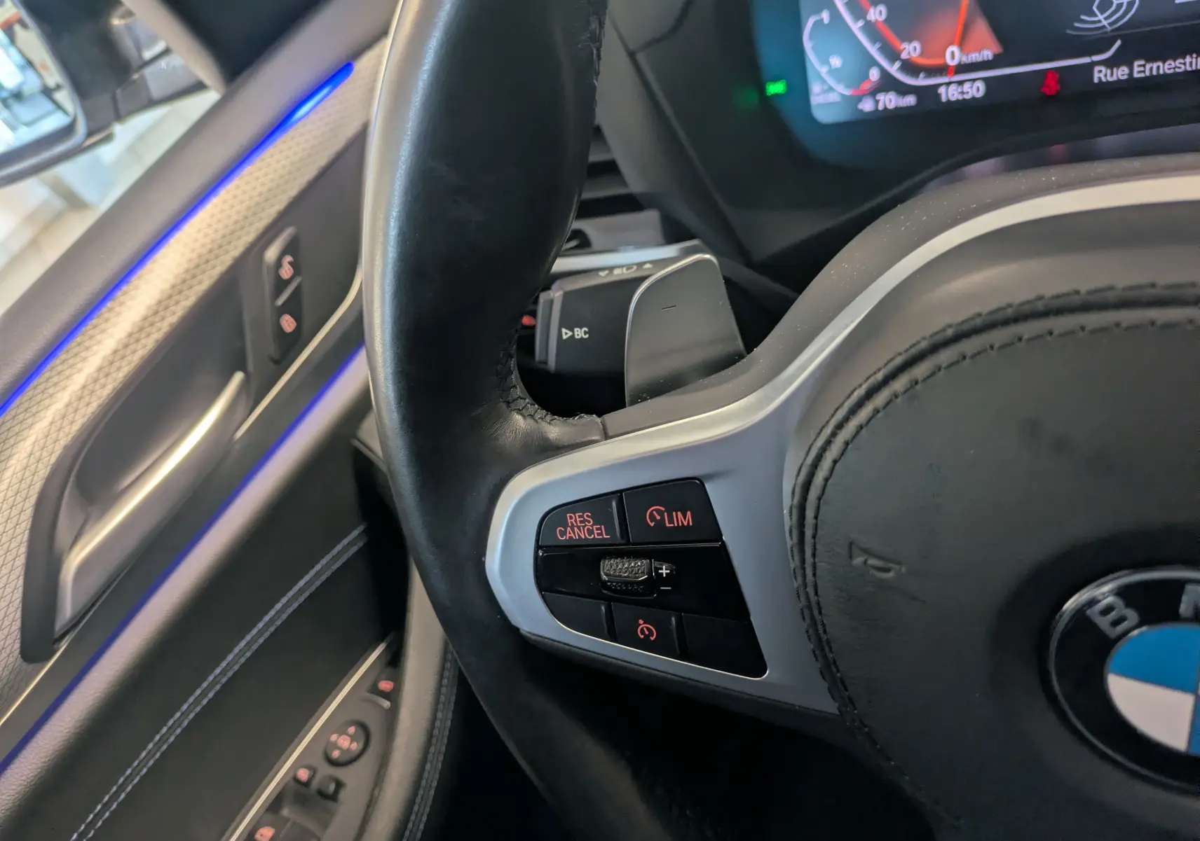 Détail du volant cuir noir avec commandes de régulateur sur la gauche, intérieur de BMW X4 blanc 2021 visible côté conducteur.