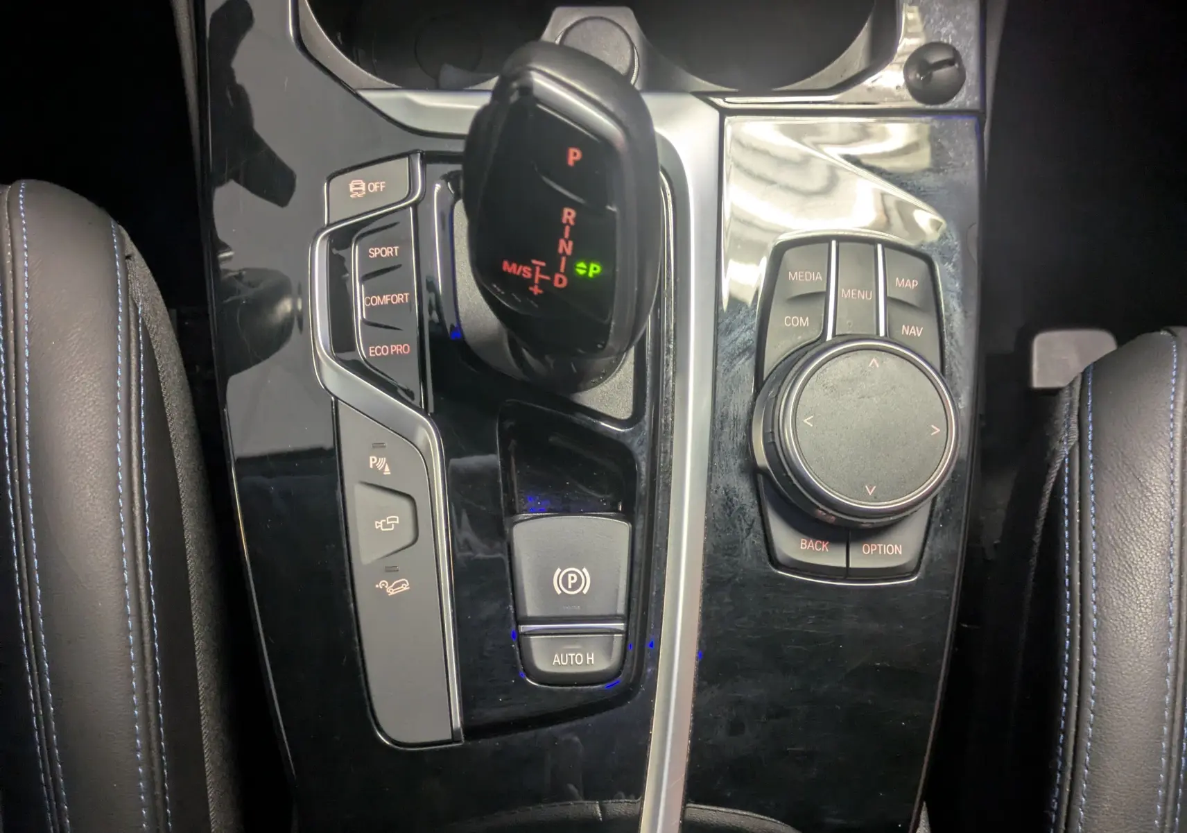 Vue rapprochée de la console centrale noire brillante du BMW X4 blanc 2021, avec levier de vitesses automatique et commandes multimédia.