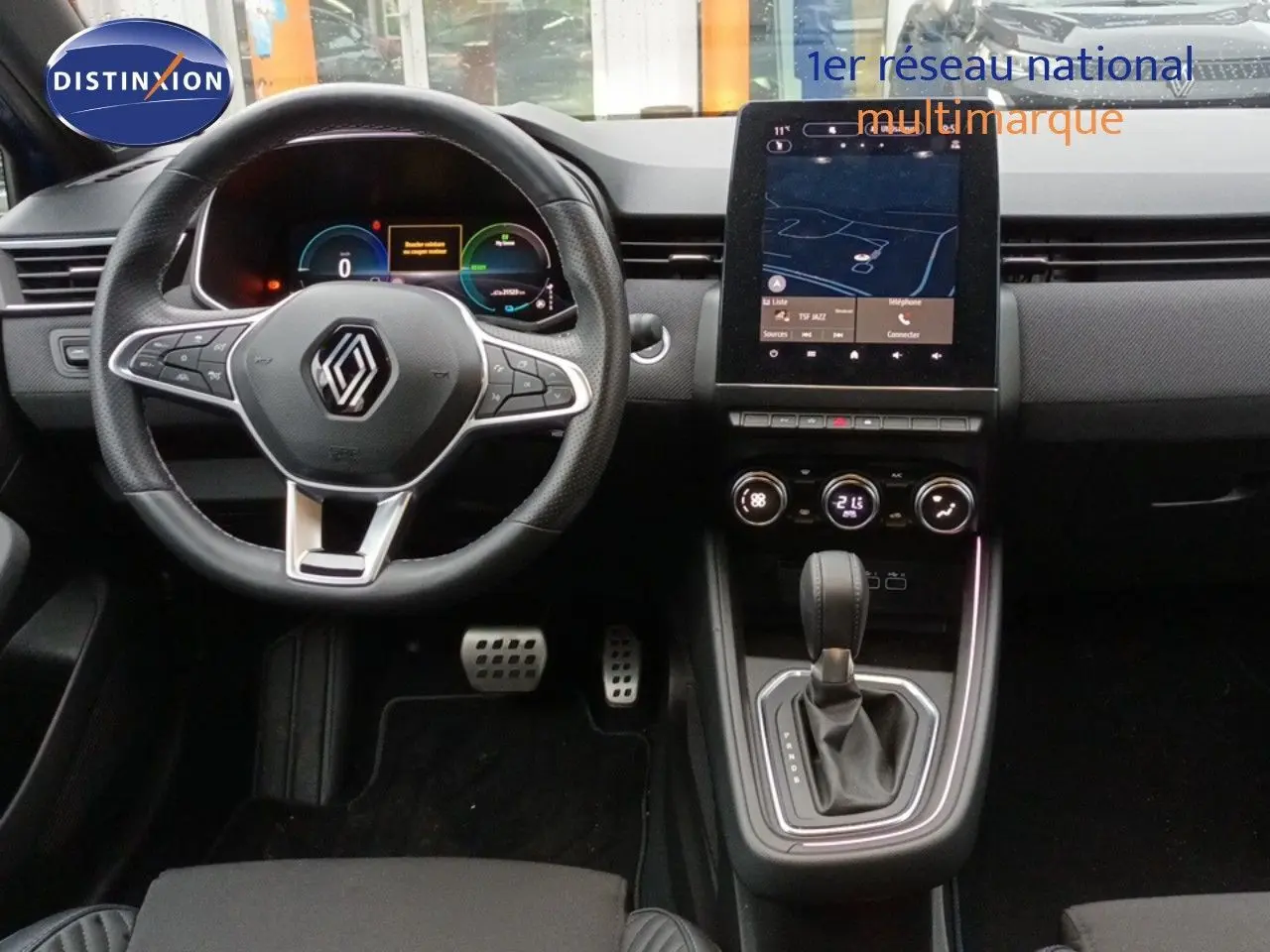Vue intérieure centrée sur le tableau de bord et volant de la Renault Clio 1.6 E-TECH 2024 avec écran tactile et levier de boîte auto.