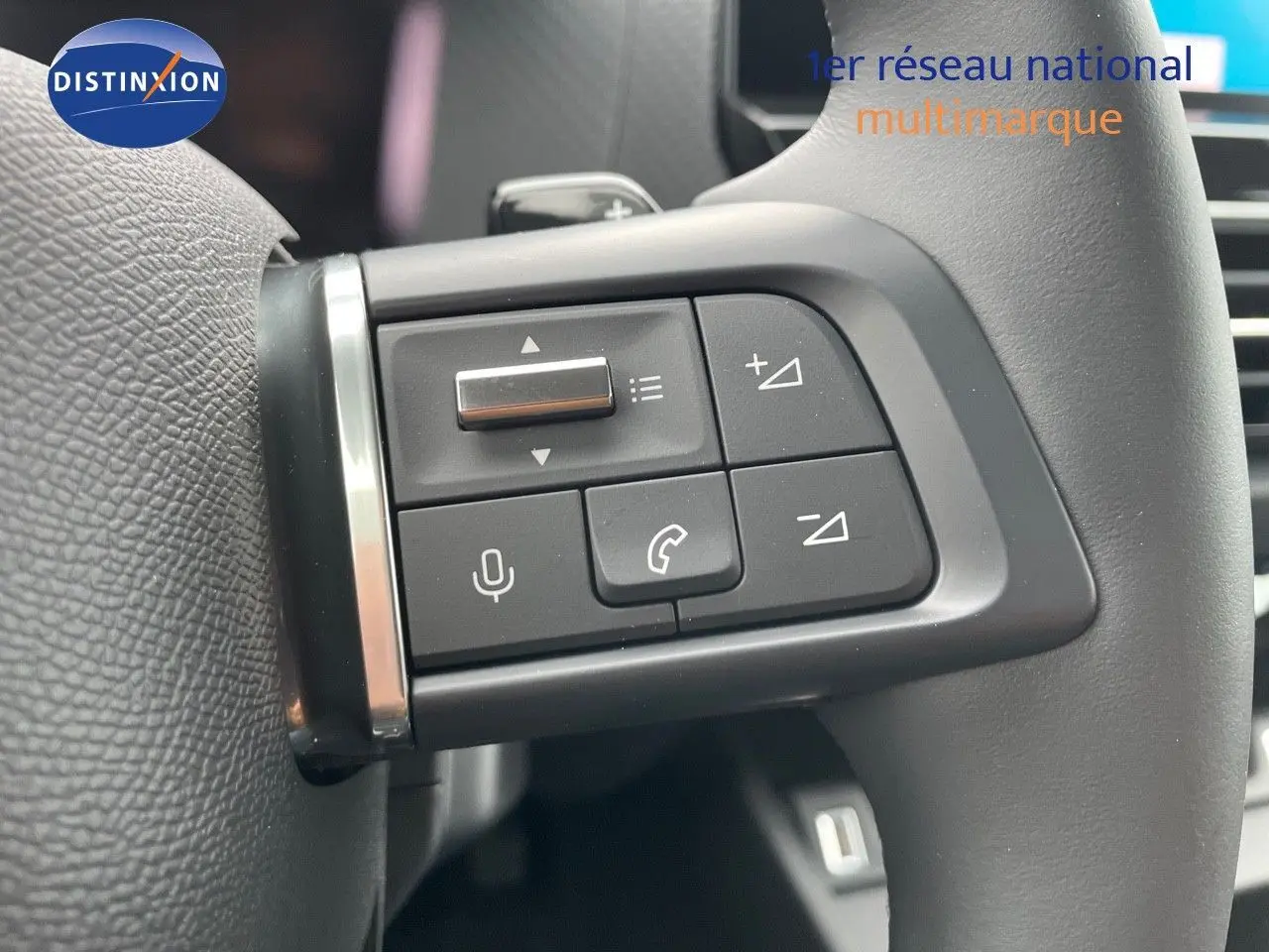 Gros plan sur les commandes du volant d'une Citroën C4 blanche métal 2024, mettant en valeur les boutons multifonctions.