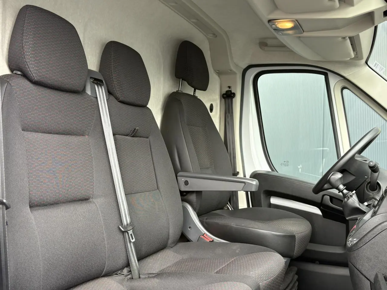 Intérieur avant du fourgon Opel Movano blanc, vue latérale sur les sièges noirs et le volant côté droit.