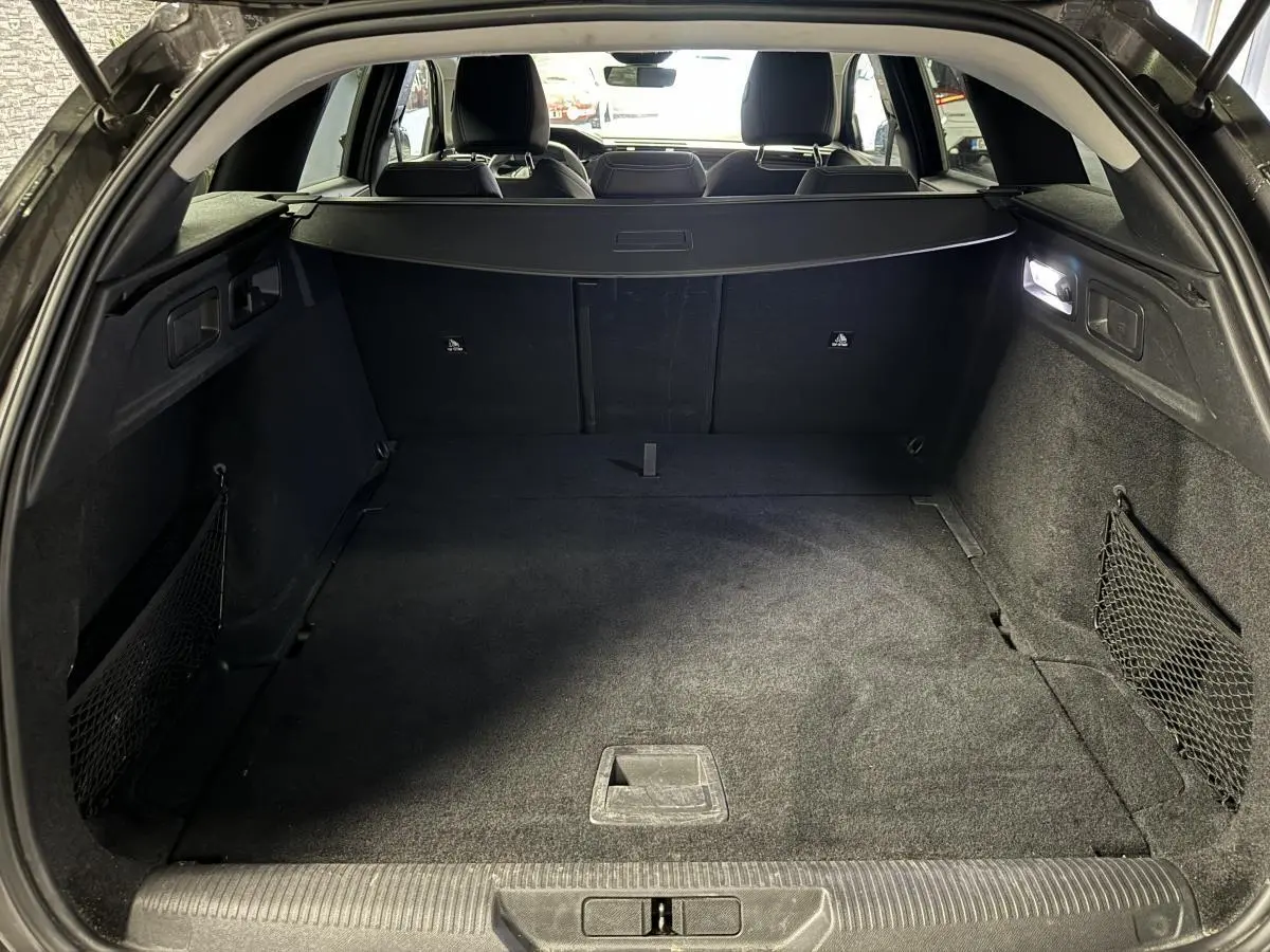 Coffre ouvert d'une Peugeot 308 SW gris, vue intérieure arrière montrant un espace de chargement propre et éclairé.